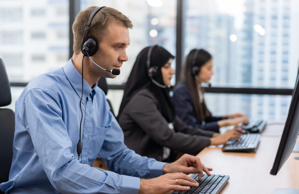 Happy smiling operator customer service agent with headsets working on computer in a call centre, talking with customer for assisting to resolve the problem with her service mind